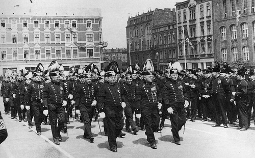 Parada grnicza w Zabrzu w roku 1935 na obecnym placu Warszawskim. rodkiem w czakach z orem defiluje dozr z kopalni pastwowej (w Zabrzu kop. Krlowa Luiza, od 1945r. Zabrze), z boku stoja szeregowi grnicy w czakach z motkami. Umundurowani w czapkach z daszkiem to uczniowie lub pracownicy biur.

